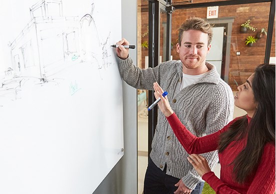 Man drawing sketch on whiteboard with coworkers reviewing