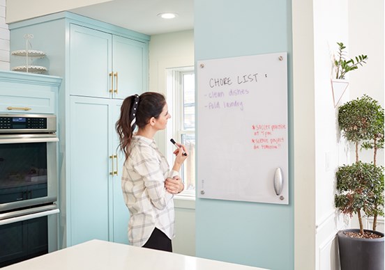 Woman in kitchen reviewing Chore List written on whiteboard