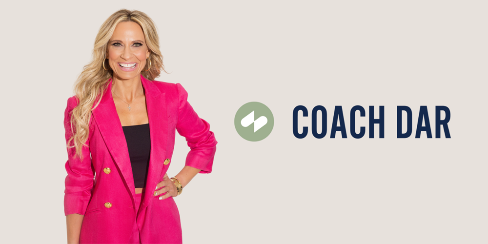 Coach Dar standing in front of a white wall with a 'Coach Dar' logo next to her.