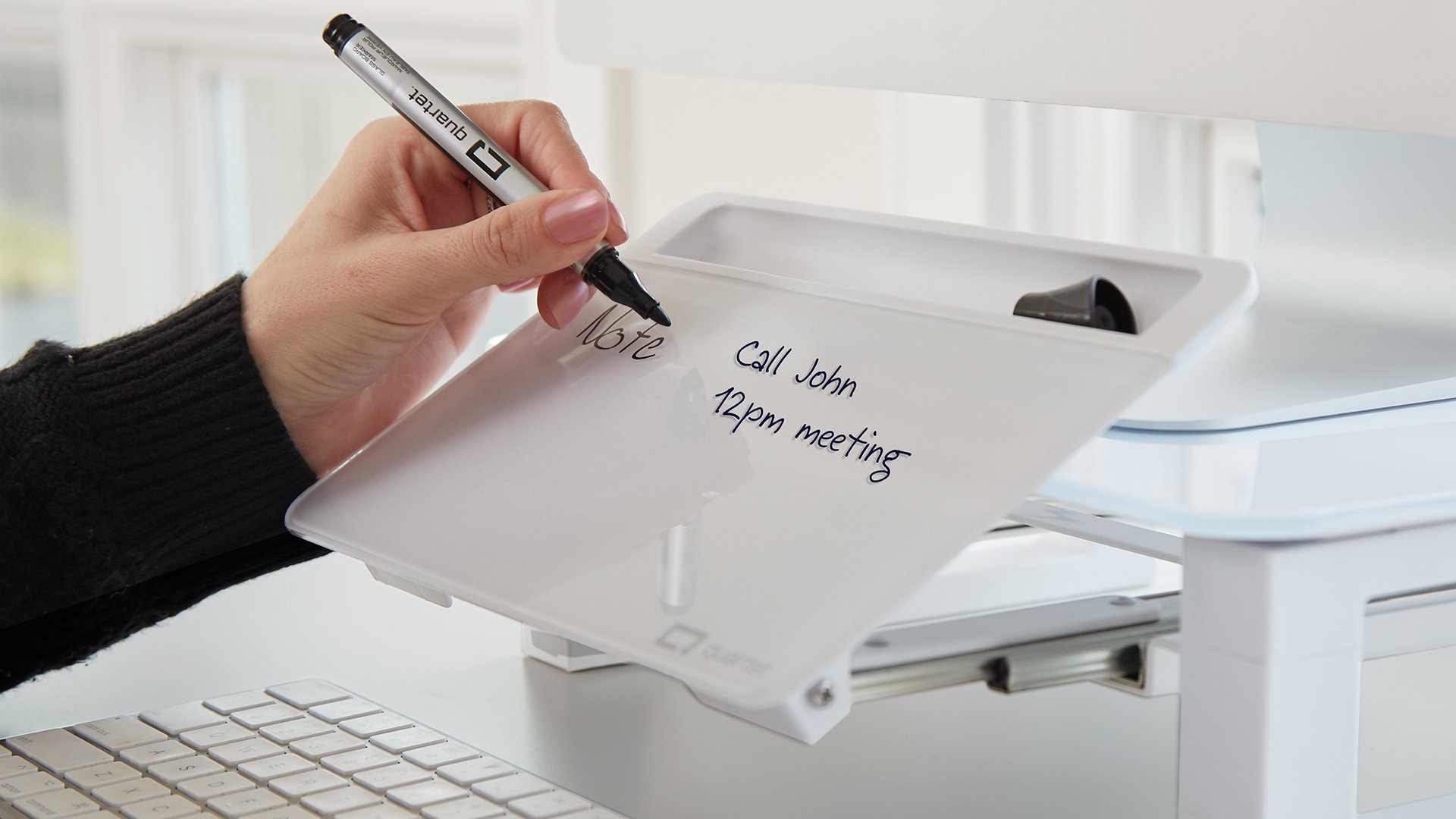Close up of a hand writing on the Glass Desktop Monitor Riser With Dry-Erase Board